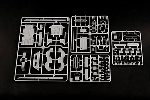 Three grey plastic model kit sprues containing various vehicle parts laid out on a black background.