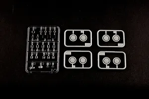 Plastic model kit sprues including one clear sprue and four grey sprues containing wheel parts on a black background.
