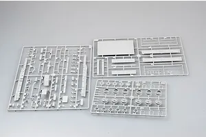 Three grey plastic model kit sprues containing various vehicle parts, including wheels and chassis components, laid out on a plain light grey background.