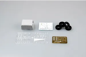 A selection of model kit parts for a Trumpeter 1/35 M1078 truck, including a cab section, decal sheet, rubber tires, clear plastic sprue, and photo-etched parts.