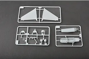Three grey plastic model kit sprues containing aircraft parts like wings and cockpit components on a dark surface.
