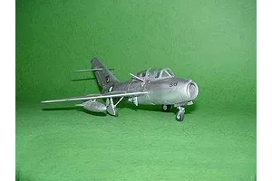 A finished scale model of a silver MiG-15 UTI jet aircraft, featuring Pakistan Air Force markings, displayed against a solid green background.