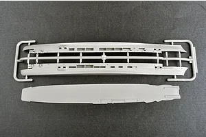 Top-down view of grey plastic model ship parts including the hull halves on a sprue and the flight deck piece for a 1/700 scale model kit.