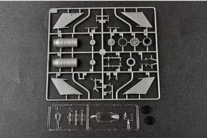 A grey plastic sprue containing aircraft model parts, a clear plastic sprue with canopy parts, and two black rubber tires on a dark grey surface.