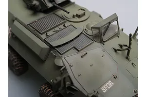 A high-angle close-up of a 1/35 scale model of a Canadian Grizzly AVGP armoured vehicle, showing the olive green hull, engine deck, and SFOR markings.