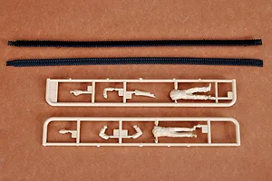 Two black rubber tank tracks and two tan plastic sprues containing model soldier parts on a brown background.