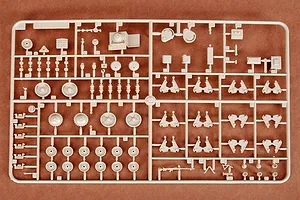 A beige plastic sprue containing various unpainted model tank parts, including wheels, suspension components, and small accessories on a brown surface.
