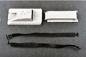 Unassembled plastic model kit parts for a Jagdpanzer E-100, including the upper hull, lower hull, and two flexible black tank tracks on a grey surface.