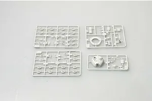Four grey plastic model kit sprues containing tank parts, including road wheels and a turret, laid out on a plain light grey background.