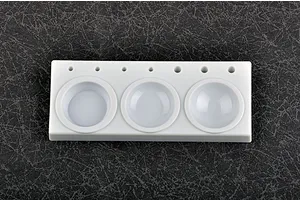 A white plastic Trumpeter modeler's paint palette with three circular mixing wells and seven small holes for holding brushes, set against a dark textured background.
