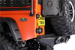 Close-up of the rear corner of an orange RC Land Rover Defender showing black GPM tail light guards installed over the lights.