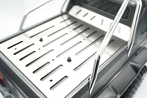 A stainless steel tray cover installed on the bed of a Traxxas TRX-6 Mercedes RC truck, featuring slotted design and chrome roll bar.