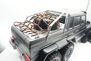 A stainless steel tray cover and brown cargo net installed on the rear bed of a grey Traxxas TRX-6 Mercedes-Benz G 63 AMG 6x6 RC crawler.
