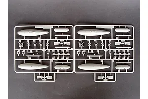 Two identical grey plastic model kit sprues containing aircraft parts like fuel tanks and small components on a dark background.