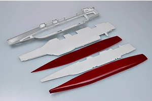 Unassembled plastic model kit parts for an aircraft carrier, including hull and deck sections in grey and red plastic.