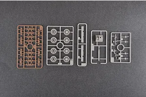 Five plastic model kit sprues for a 1/35 scale tank, including wheels, turret parts, and suspension components, laid out on a dark grey surface.