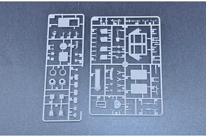 Two grey plastic model kit sprues containing various vehicle parts laid out on a dark surface.