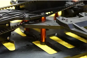 Close-up of orange anodized aluminium spacers installed on an RC car chassis with black plastic components and a drive belt.