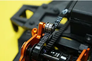 Close-up of an orange anodized aluminium belt tensioner installed on an RC car chassis with a black drive belt.