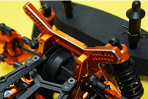 Close-up of an orange anodized aluminium shock tower and suspension components installed on an RC car chassis.