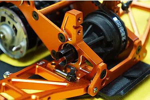 Close-up of orange anodized aluminium RC car chassis parts installed on an HPI Sprint 2, showing suspension arms and drivetrain components.