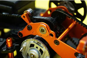 Close-up of orange anodized aluminium RC car chassis components including motor mount and belt drive system.