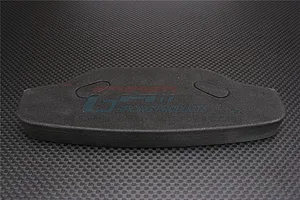 A black urethane foam RC car bumper by GPM Racing, shown from a top-down perspective on a carbon fiber textured surface.