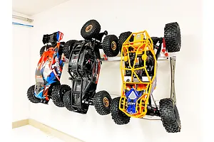 Three RC cars mounted vertically on a metal wall rack against a white wall.