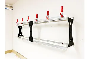 A T-Bone RC car wall rack mounted on a white wall, featuring aluminum rails, black side supports, and five adjustable red-tipped pegs.