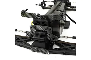 A close-up view of a carbon fiber rear camber link mount installed on an RC car chassis, showing the weave pattern and mounting hardware.