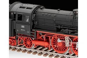 Close-up of a 1/87 scale plastic model steam locomotive with a matte black boiler and bright red wheels on a model railway track.