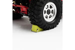 A yellow alloy tyre stopper placed under the front wheel of an RC crawler vehicle on a white background.