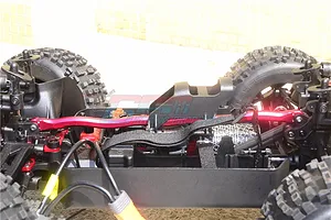 A red aluminium centre brace bar installed on an RC car chassis, showing the central structural component between the front and rear suspension towers.