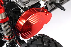 A red anodized aluminium transmission gear cover installed on an RC car chassis, featuring a machined chevron pattern.