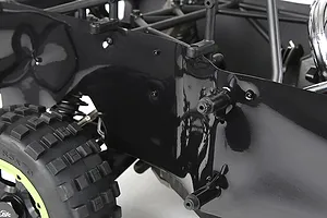 Close-up of a black plastic dust guard installed on the side of an RC buggy chassis, showing the mounting points and nearby off-road tire.