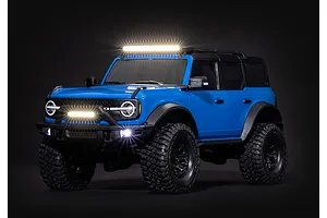 A blue Traxxas RC Ford Bronco model vehicle featuring an illuminated roof-mounted LED light bar and front bumper lights against a black background.