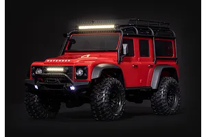 A red Traxxas Land Rover Defender RC crawler featuring an illuminated roof-mounted LED light bar and front bumper lights against a black background.