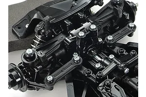 Close-up of the black plastic front suspension assembly of a Tamiya TT-02 RC car chassis, showing steering linkages, shock towers, and screws.