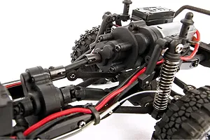 Close-up of the chassis and drivetrain of an Element RC Enduro24 rock crawler, showing the motor, transmission, suspension, and driveshaft.