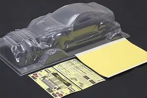 An unpainted clear polycarbonate RC car body shell of a Nissan GT-R R35 with included decal sheets and masking tape on a black background.