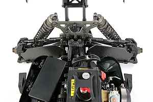 Top-down view of an RC car chassis showing carbon fibre front suspension arm guards installed.