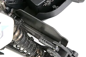 Close-up of a carbon fibre suspension arm guard installed on an RC vehicle chassis.