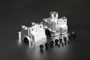 Two silver aluminium RC gearbox case halves and a set of black mounting screws arranged on a dark background.