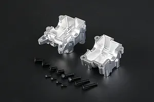 Two silver aluminium RC gearbox case halves with a set of black mounting screws on a dark background.