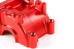 A close-up view of a bright red anodized aluminium RC gearbox case component with visible machining marks and mounting holes.