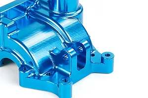 A close-up view of a bright blue anodized aluminium RC gearbox case showing machined surfaces and mounting points.