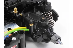 Close-up view of the Tamiya MB-01 chassis front suspension assembly, showing black plastic arms, a coil-over shock, and steering linkage.
