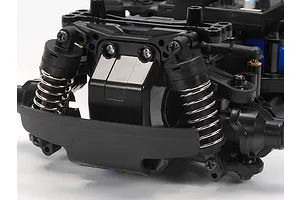 Close-up of the front suspension and bumper assembly of a Tamiya MB-01 RC car chassis, featuring black plastic parts and silver coil springs.