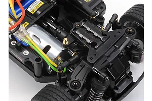 Close-up of a Tamiya MB-01 RC car chassis showing the electric motor, suspension components, and wiring on a white background.