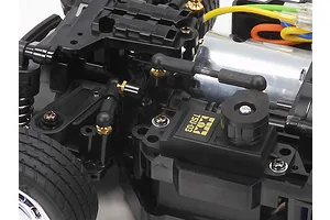 Close-up of a Tamiya MB-01 RC car chassis showing the TSU-03 steering servo, electric motor, and suspension linkages.